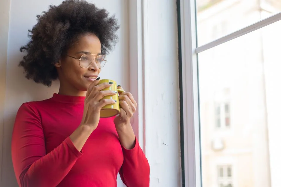 Mulher pensativa com um café, junto à janela com luz da manhã